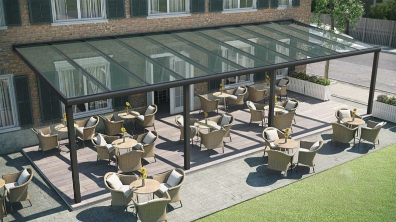 Vista dall'alto di una Veranda moderna nero 9005, dimensioni 12,06 x 4,0 metri con tetto in vetro trasparente. Pergola/Gazebo elegante e resistente alle intemperie, ideale per spazi esterni raffinati e confortevoli, offre protezione UV ed è facile da montare.