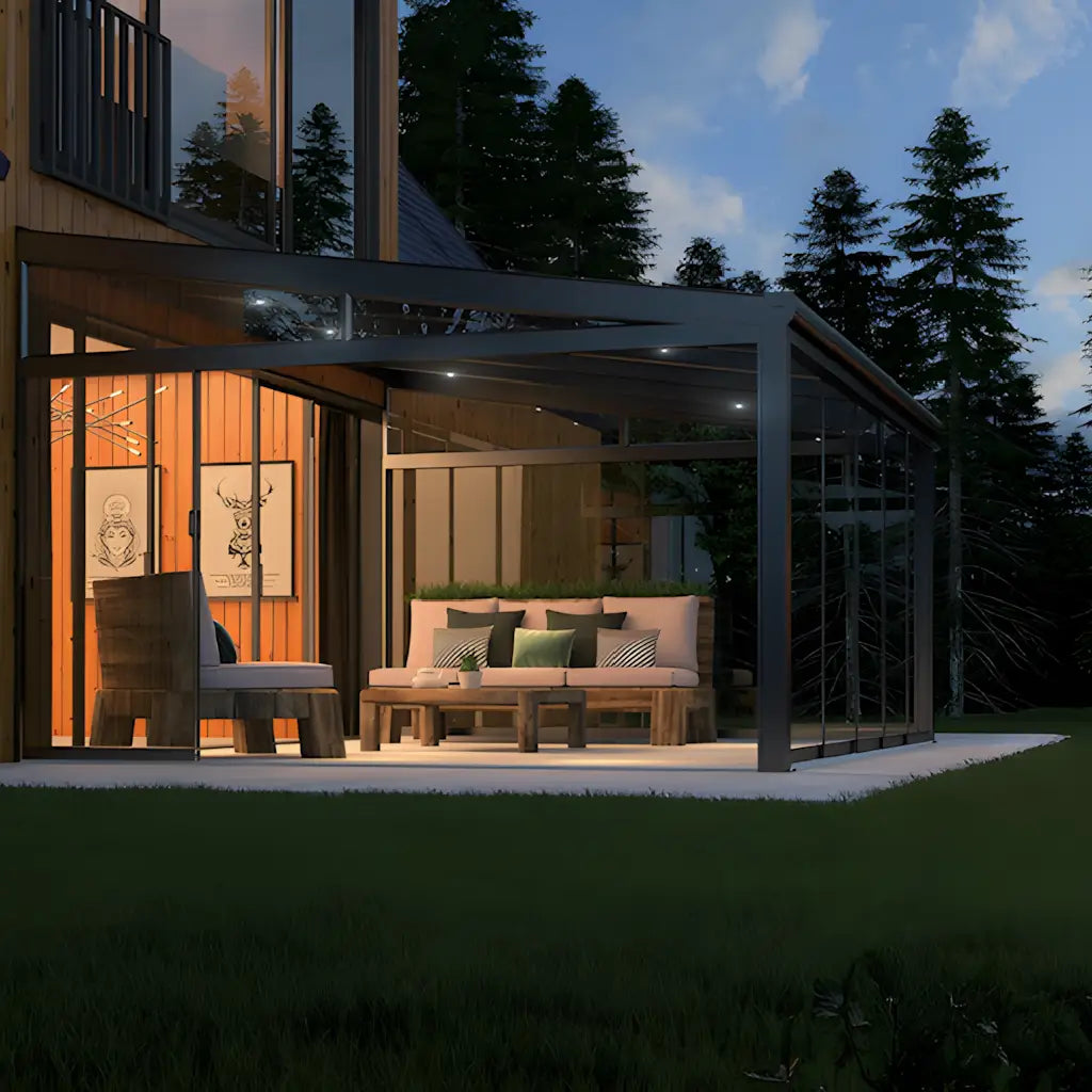 Veranda in alluminio antracite di sera con tetto in policarbonato opale; area relax illuminata, vetrate scorrevoli opzionali – Verande in Giardino.